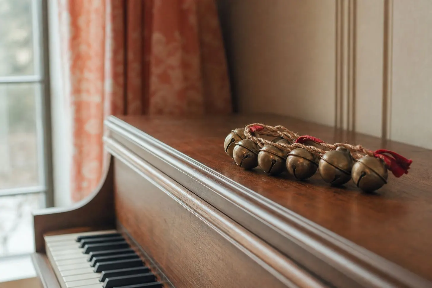 A small strand of vintage sleigh bells resting on the closed lid of an upright piano, soft window light, no hands in frame